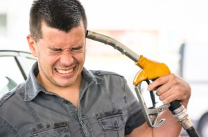 Frustrated driver holding gas pump nozzle to his head, illustrating the pain of high fuel prices in California